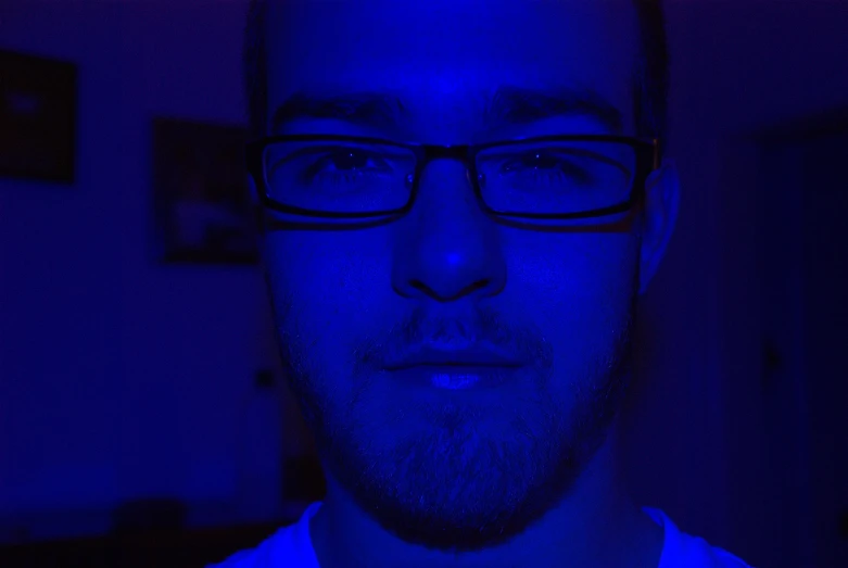 a man with glasses and a blue light in the dark