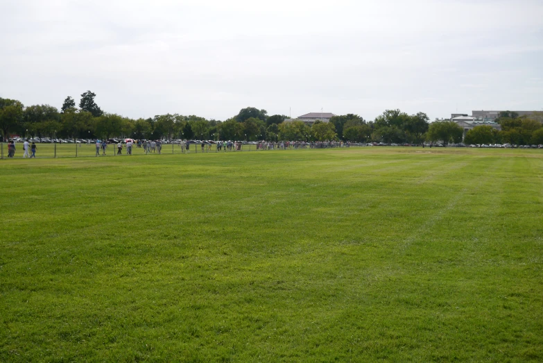 several people in the distance and one on the far side watching a plane flying through the sky