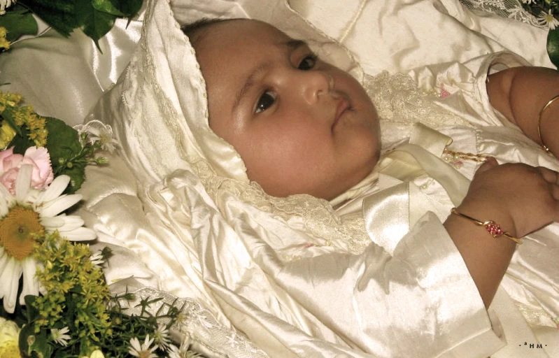 a little baby in a white dress laying on top of flowers