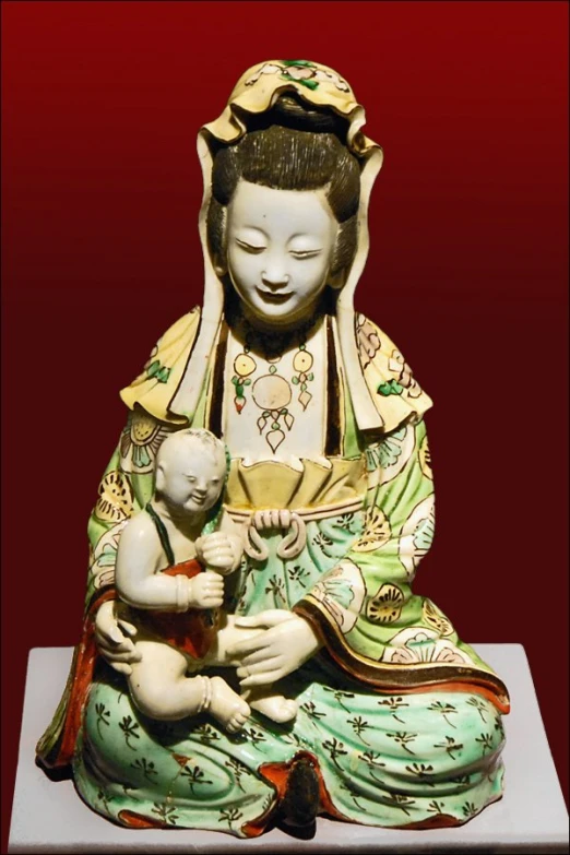 a statue holding a baby in her lap with a red wall in the background