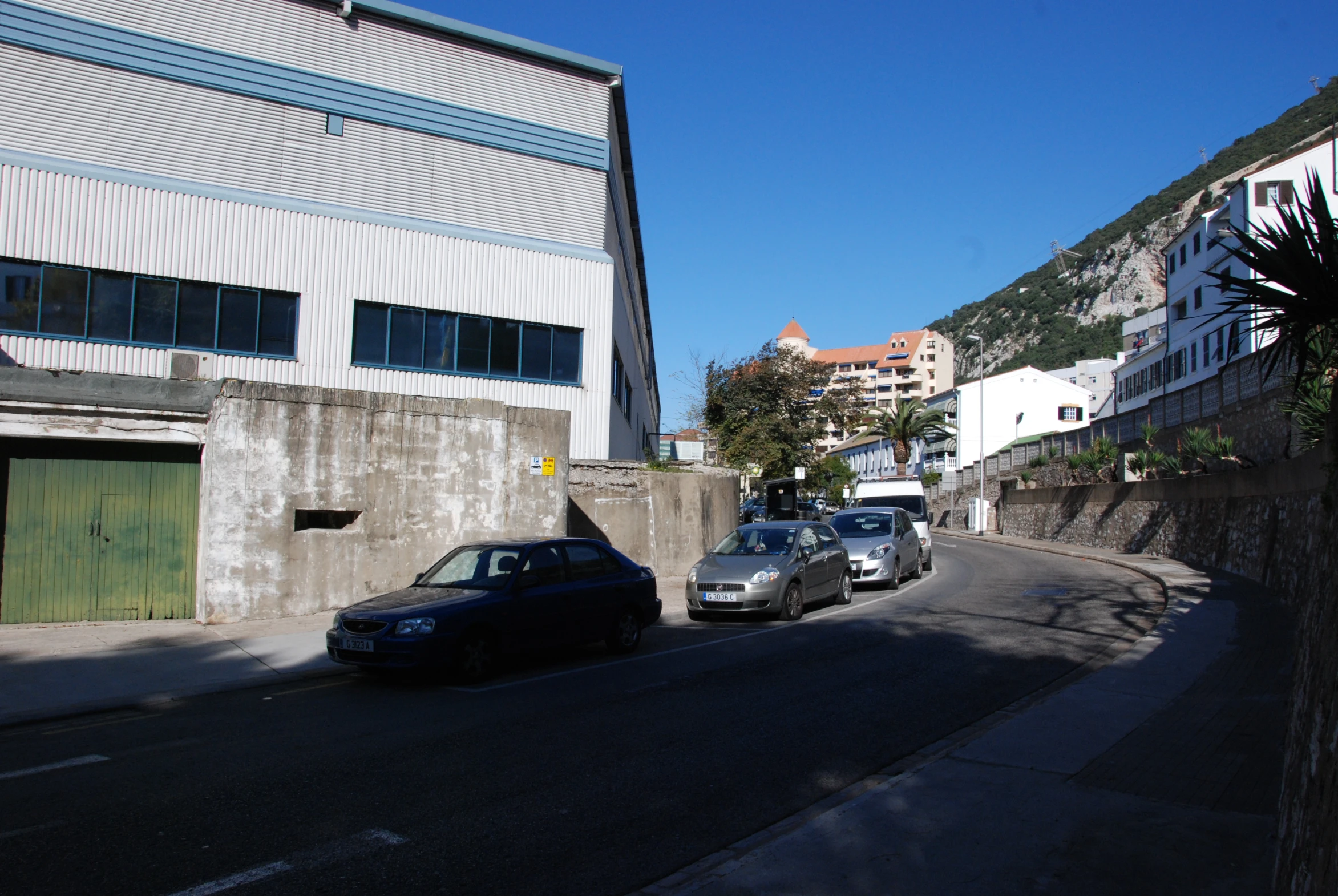 cars are parked in front of a grey building on a hill side