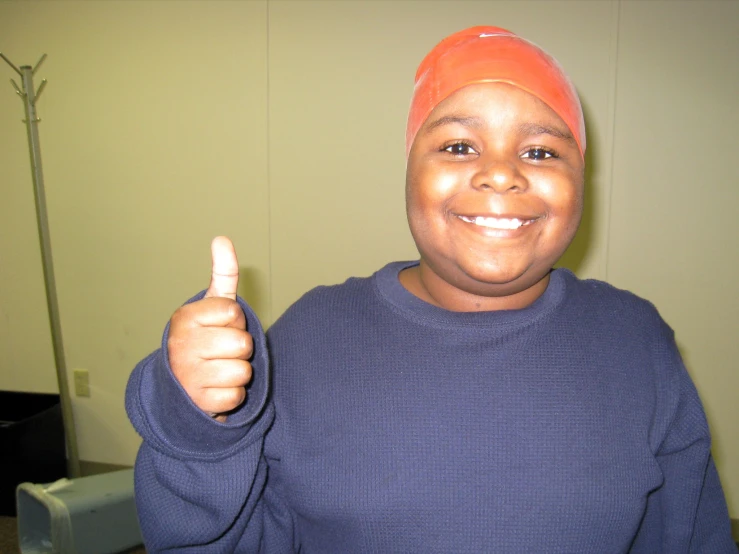 a child with an orange hat on giving a thumbs up