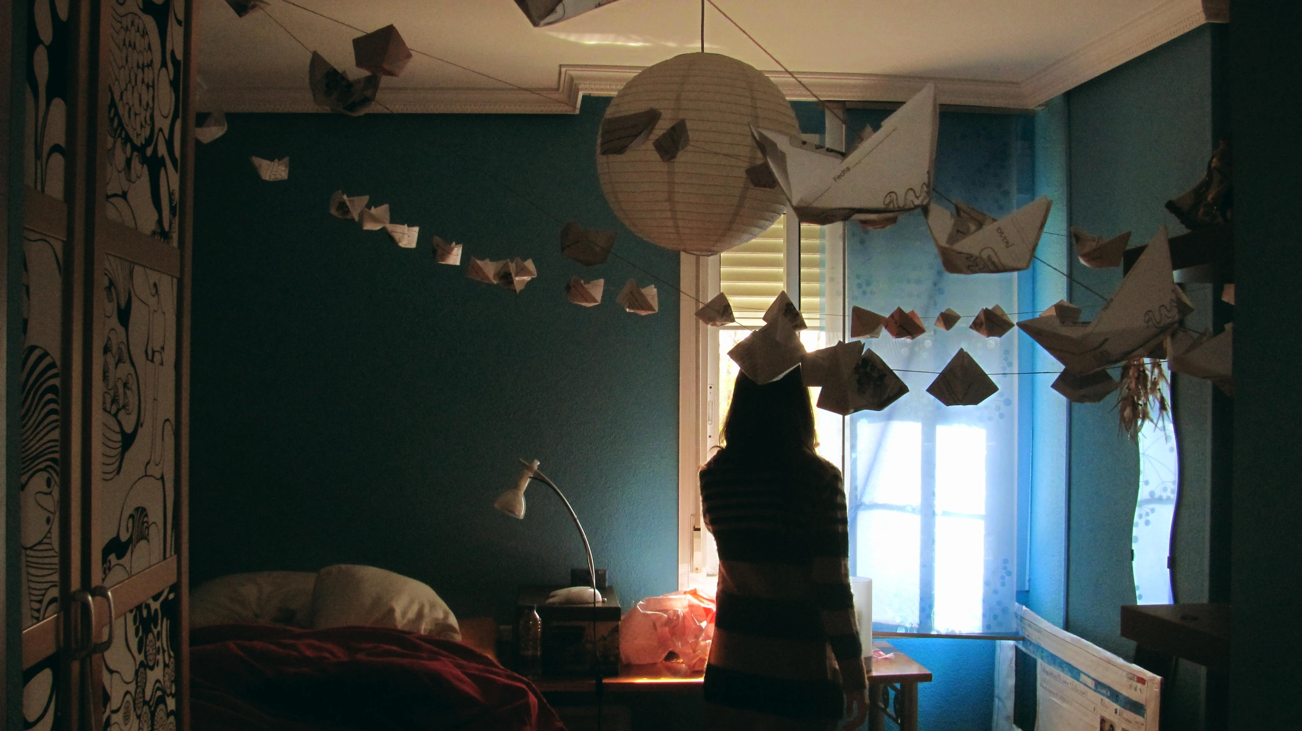 a cat stands in a dark room as a paper lantern is hanging from the ceiling