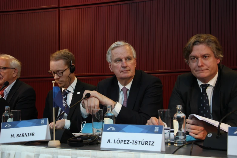 three men in business suits at a table with microphones