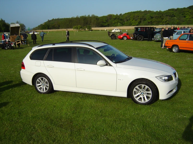 a white bmw car parked on the side of a field