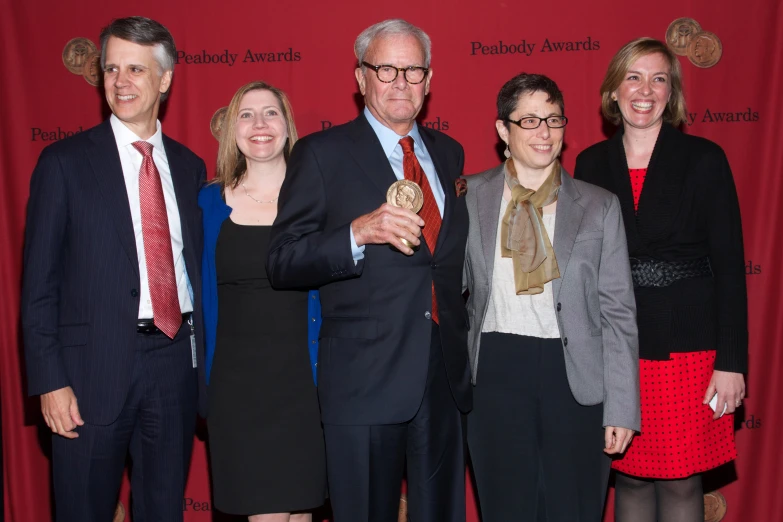 five people standing next to each other in front of a red backdrop