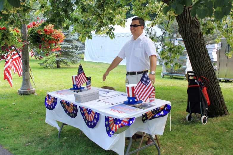 a man in white shirt standing next to a table with american flags
