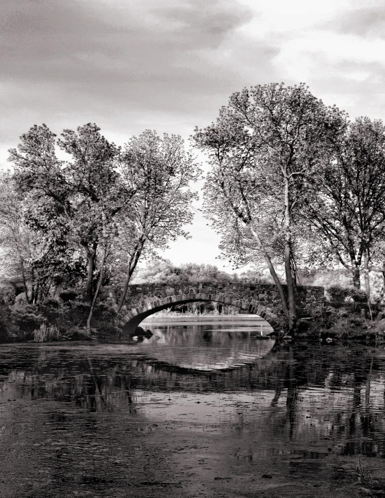 an old bridge over water with trees reflected in the water