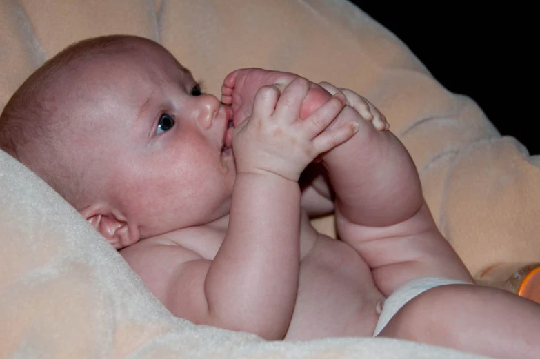 a baby sitting on a bed covered with a blanket