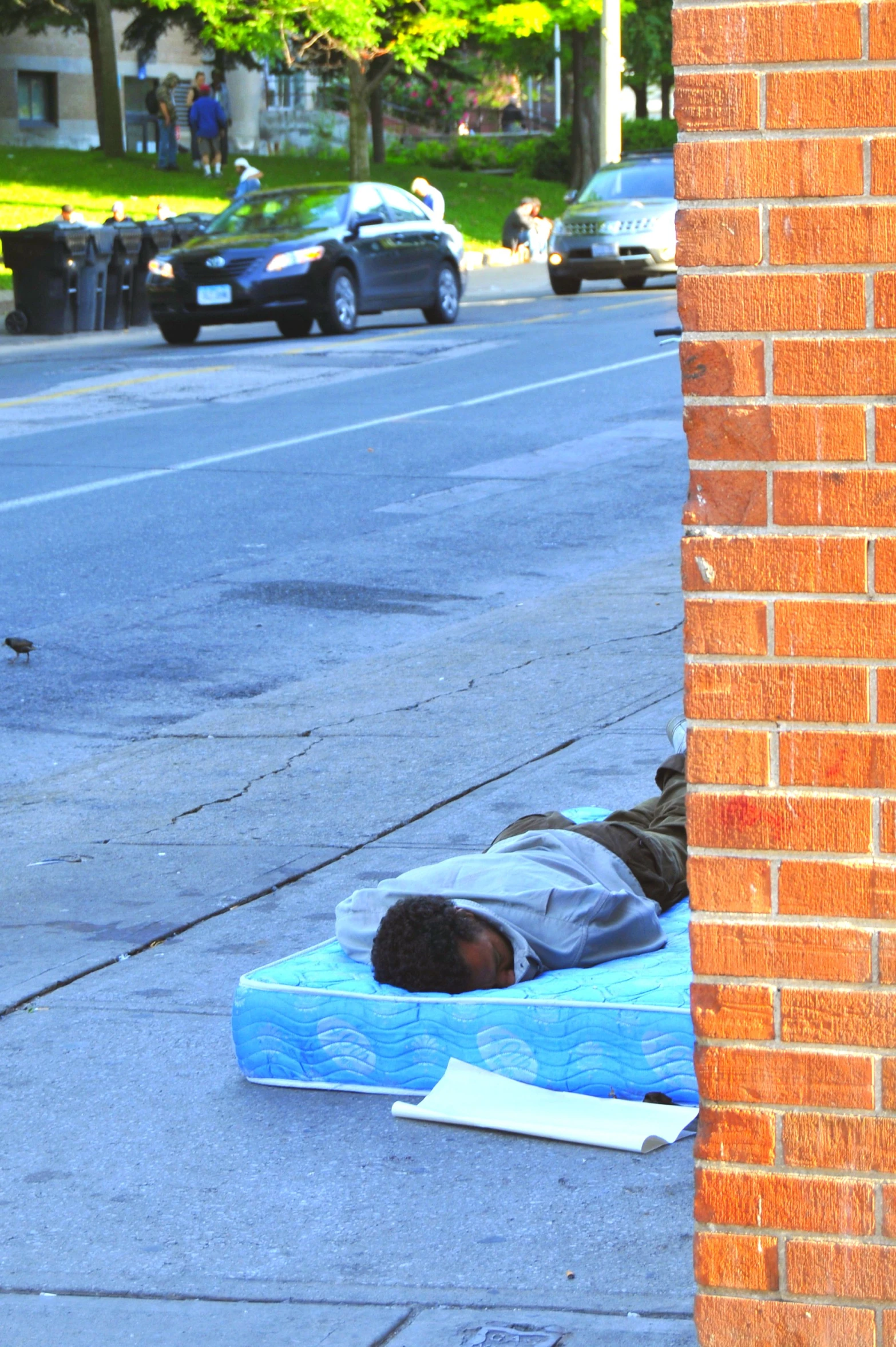 a man sleeping on a mattress near a city street