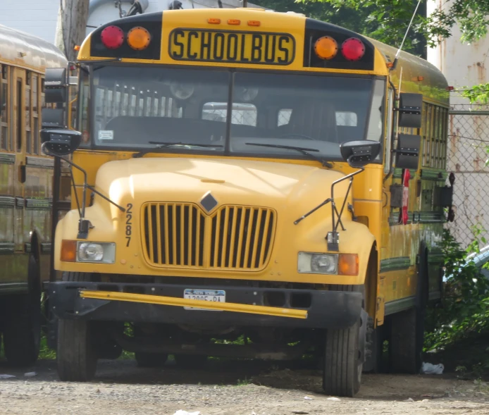 the school bus is parked on the gravel by the fence