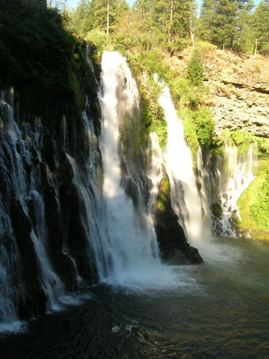 a waterfall with trees around it with people standing at the top