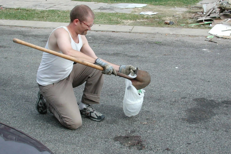 a man squatted on the ground holding a shovel over a trash can