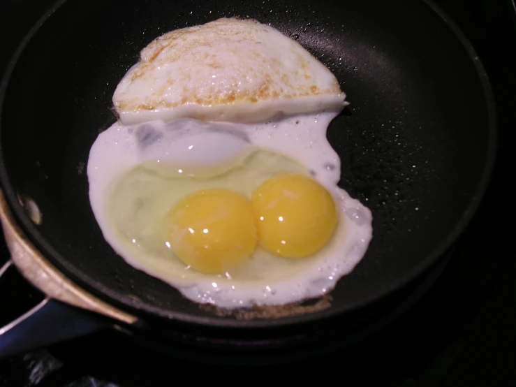 two fried eggs with a piece of meat in a pan