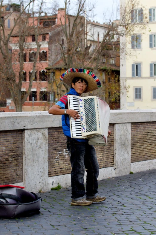 a man with a mexican hat holds a accordine while standing on a bridge