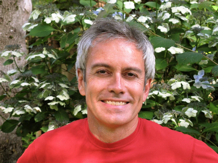 an older man with gray hair smiles near a bush