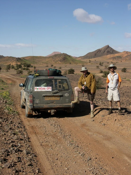 two men standing next to an suv in the desert