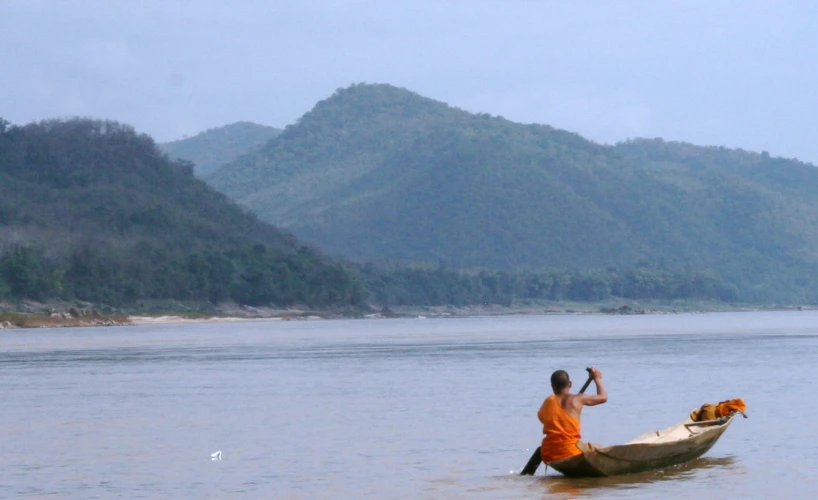 man on canoe in large body of water with mountains in background