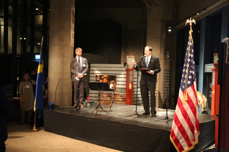 two men in suits stand at podiums speaking