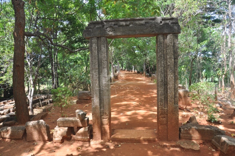 a path leading through a stone archway to trees