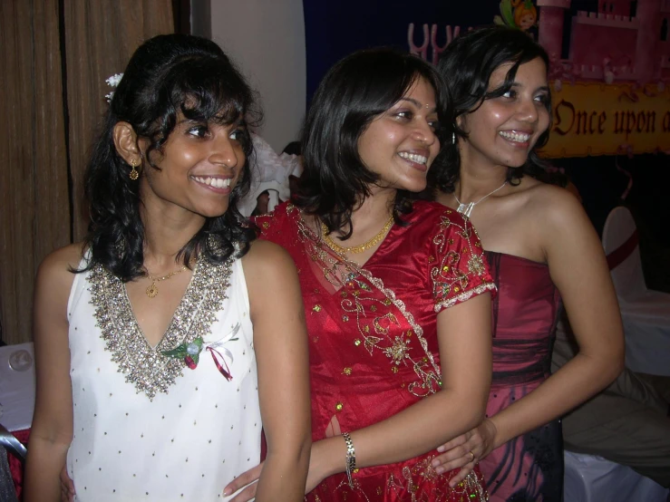 three young women in dresses smile together