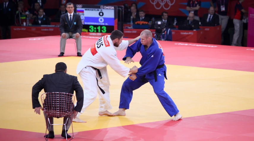 three men stand around a man in blue on a sumo ring