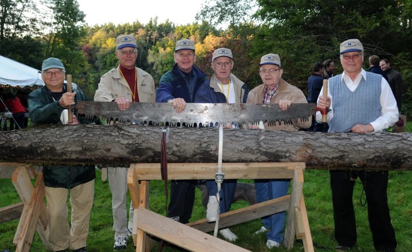 four people standing around a tree trunk with saw marks