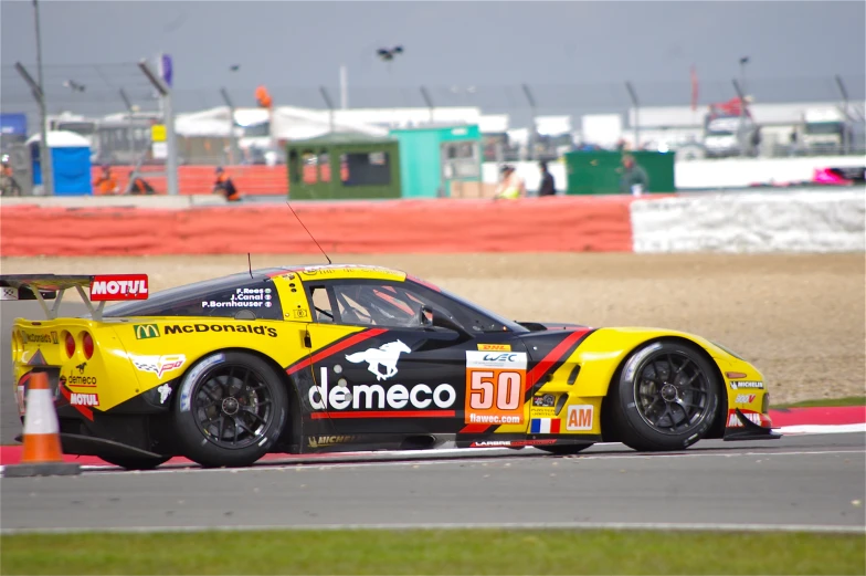 a yellow race car with black lettering is at the start of a racetrack