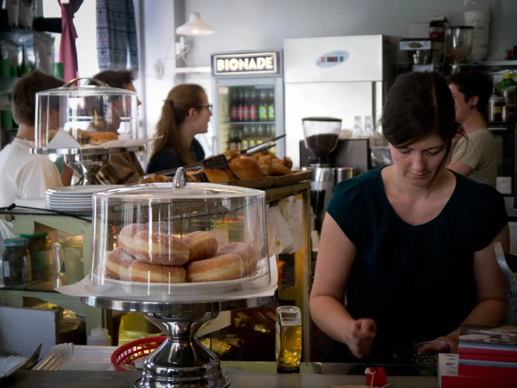 woman preparing a donut at a bakery behind a glass case