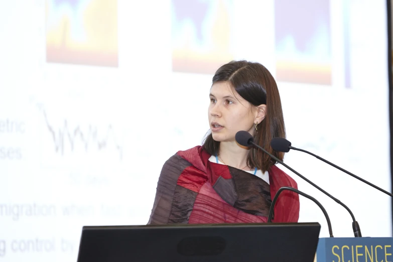 a woman in red sits in front of a microphone and a podium