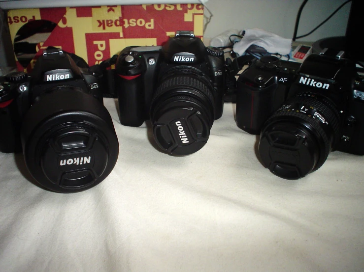 six cameras, some with the top lens pointed at them, all standing on a bed