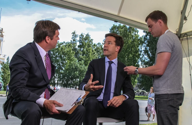 a man in suit talks to two men in a white tent