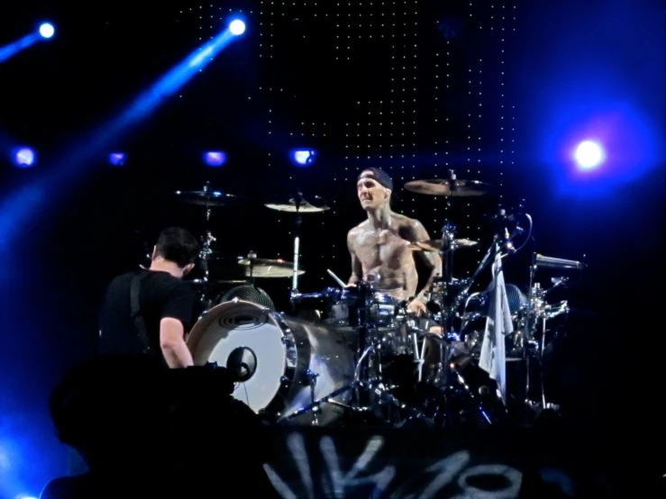 a shirtless man playing on drums while other people watch