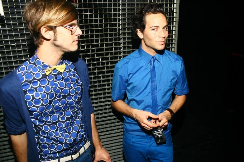 two men in blue shirts and bow ties standing together