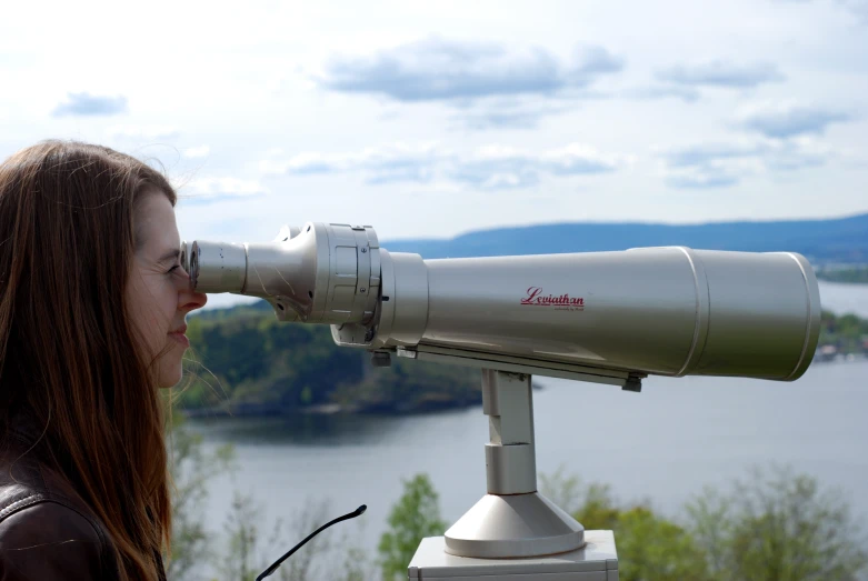 a woman looking through a telescope while standing next to some trees