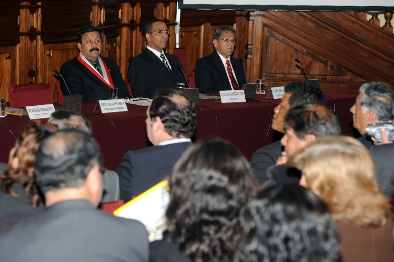 men sitting in a row behind red chairs in a auditorium