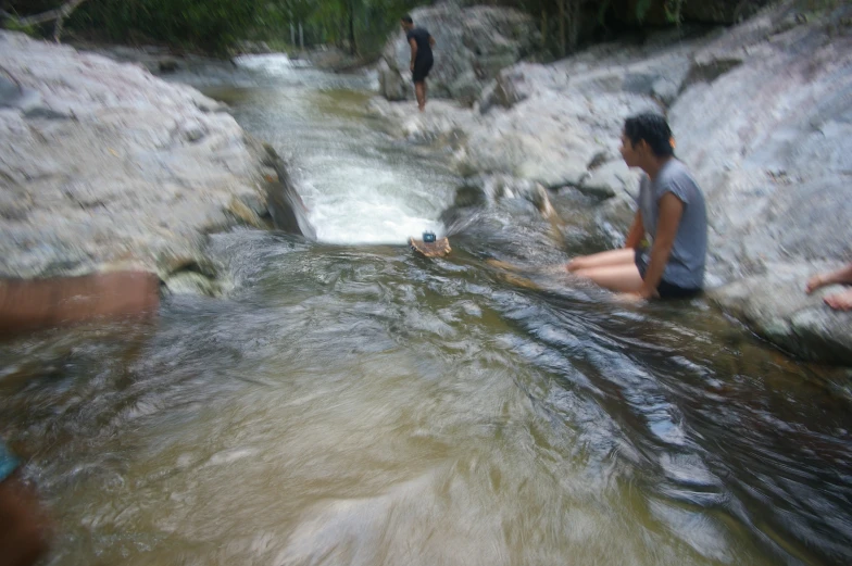 two people sit on rocks and look at a creek