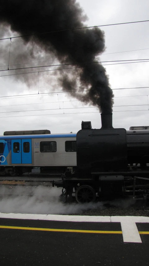 a train with a train engine emits smoke as it travels down the tracks