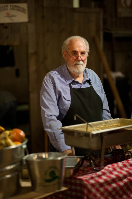 an old man wearing a black apron while standing behind a buffet table