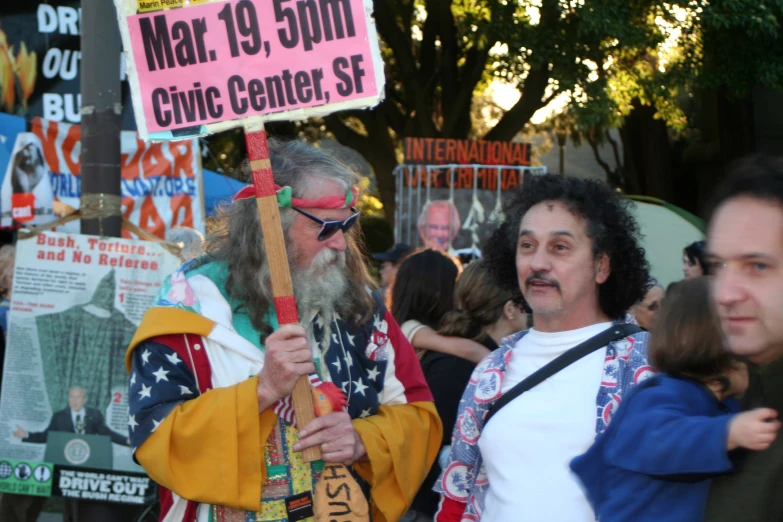 a man wearing glasses and an orange coat is holding a sign in front of a crowd of people