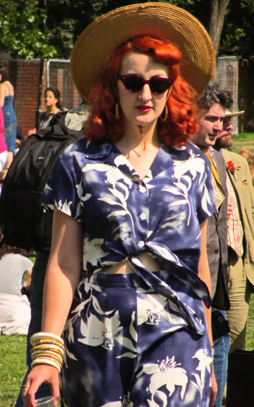 a woman with red hair wearing a blue floral dress and a large hat