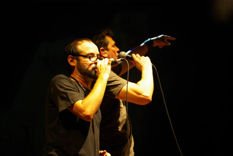 two men on a stage one with his arm around the other's neck and one singing