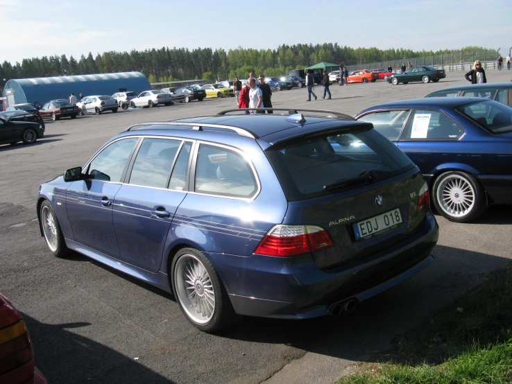 many cars and people stand around in the parking lot