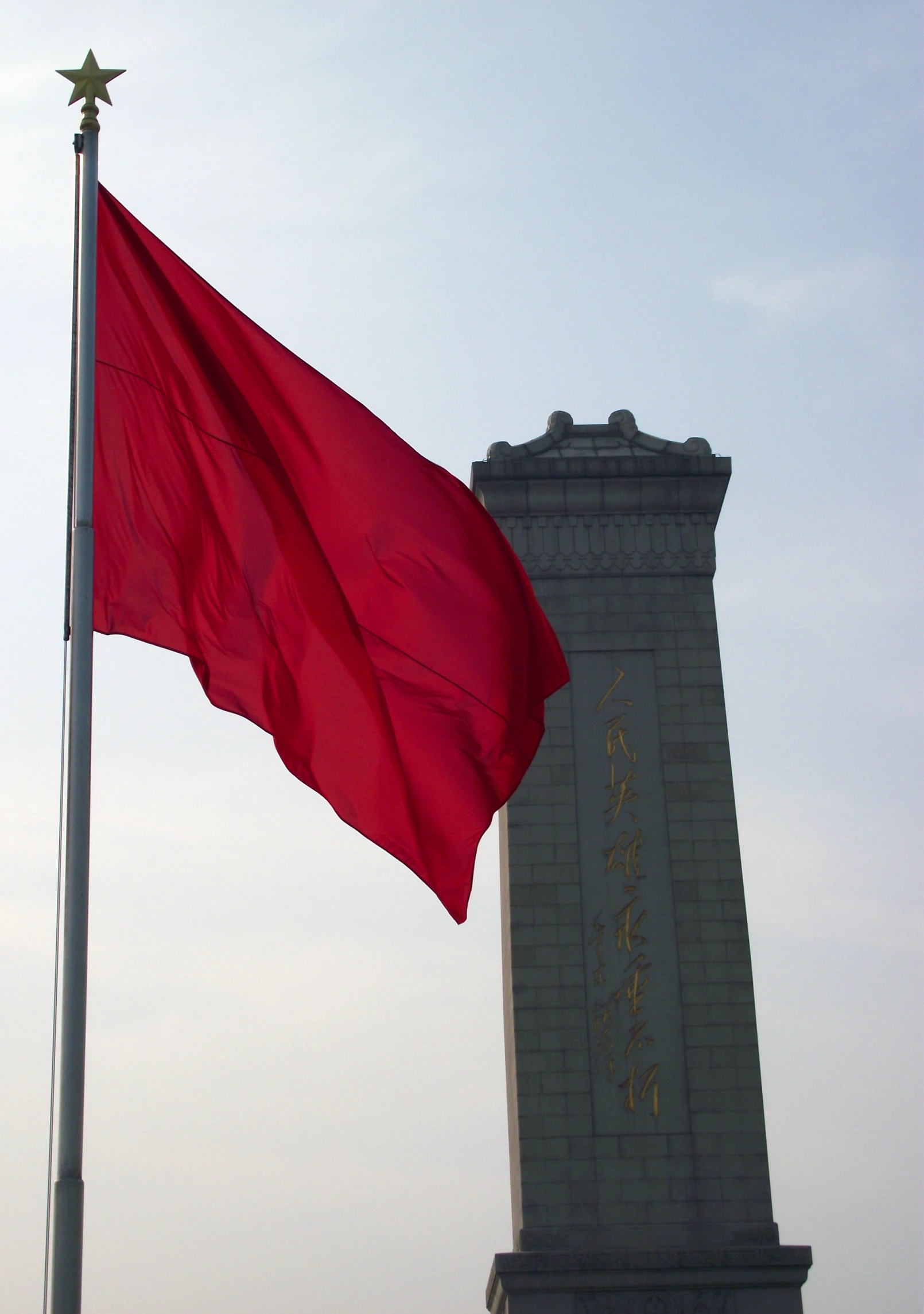 an old chinese flag flies next to the statue