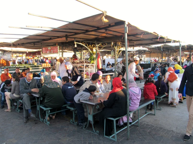 many people sitting under umbrellas at an outdoor market