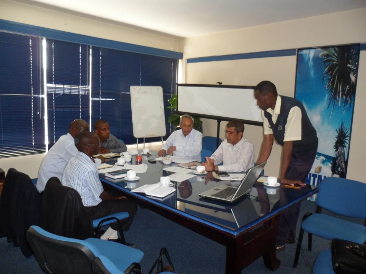 a man stands at a board while the other men are seated at the table