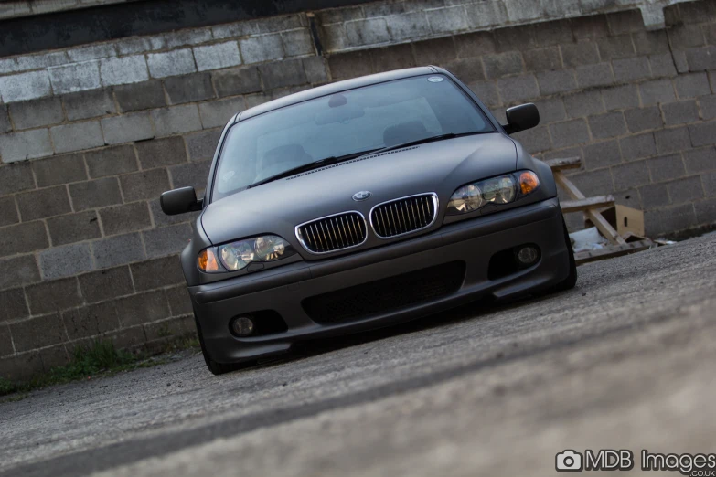 the front end of a black car parked by a brick wall