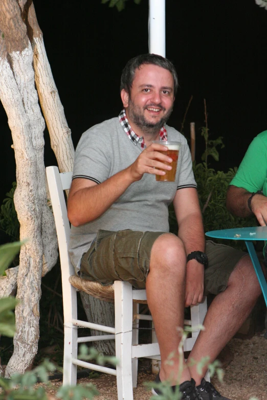 the man is sitting in a chair smiling holding up a beer