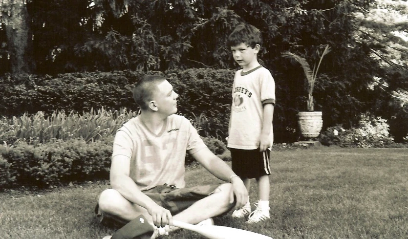 a man sitting on a lawn with a child standing behind him