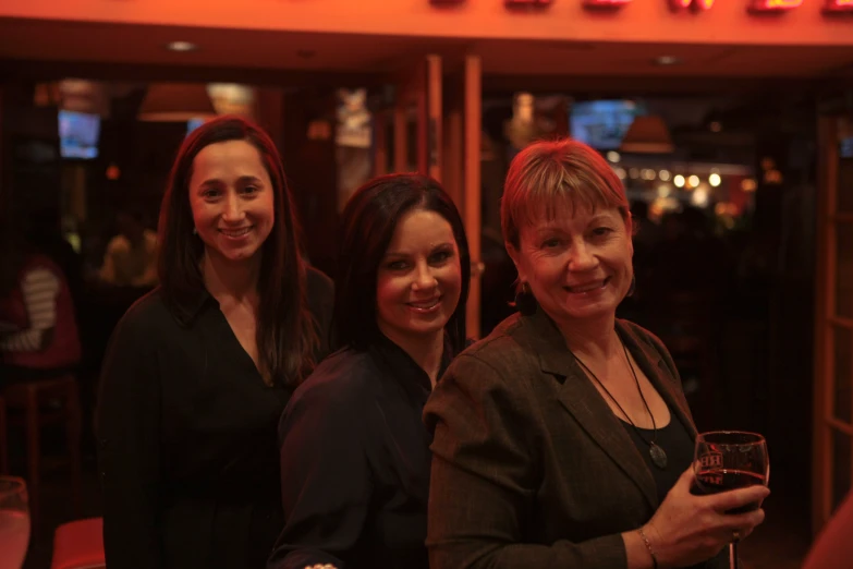 three woman pose together outside of the bar with wine